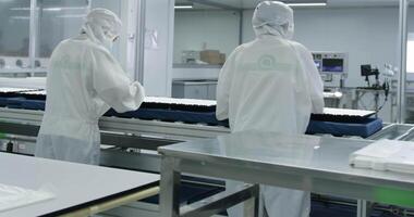 Workers in protective gowns, gloves and masks work on a conveyor belt for the production of computer monitors. video