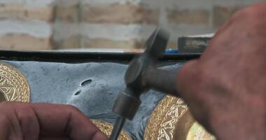 ein Meister Prägegerät schafft ein Muster auf ein Kupfer Teller mit uralt Technologien. video