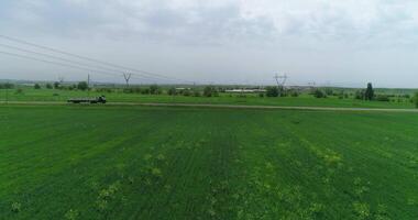 The drone flies on a country road with a truck on it. There are green fields and trees around. video