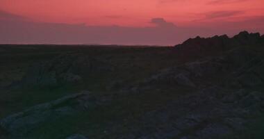 Visão do rochoso colinas com arbustos e Relva contra uma nublado pôr do sol céu video