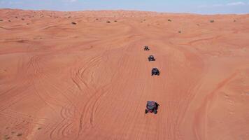 A drone flies over a caravan of buggies driving through the desert sand video