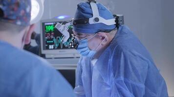 a cirurgião vestindo especial óptica supervisiona a Operação. saúde monitor em a costas video