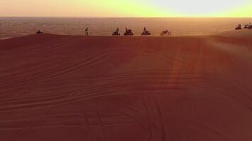 ein Drohne fliegt Über atvs Stehen auf das Sand Dünen von das Wüste gegen das Hintergrund von das Sonnenuntergang video