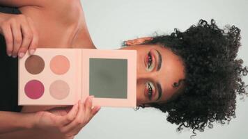 un joven mujer con brillante maquillaje se ríe y se regocija, participación un conjunto de productos cosméticos en su mano video