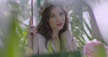 Young girl in a wreath of flowers swings on swing video