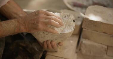 A pottery master holds a stone of clay in his hands for the production of dishes in his workshop video