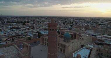 The drone flies around the minaret of the architectural complex Poi-Kalon. In the background are the old houses of Bukhara, Uzbekistan. Early cloudy morning video