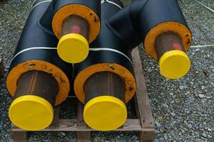 Black  isolated heating pipes with yellow plastic plugs lie on a construction site. photo