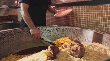 The chef puts carrots with a slotted spoon in a plate with rice from a large cauldron for pilaf video