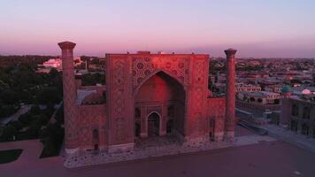 A drone flies near a complex Bibi-Khanym Mosque in Samarkand, Uzbekistan. The building is illuminated by the pink dawn light. Cloudless morning. video