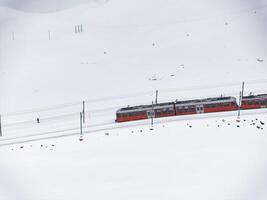 brillante rojo tren en Nevado paisaje con caminante, zermatt esquí recurso zona foto