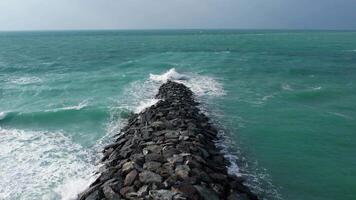 A wave rolls down a rock breakwater off the shore video