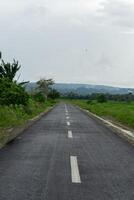 Empty asphalt road with mountain view in the background.  Roadway view in Aceh Besar, Indonesia. photo