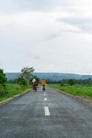 Two hijab Asian woman riding bicycle at the morning on the asphalt road. Two girls cycling with mountain and paddy rice field view photo