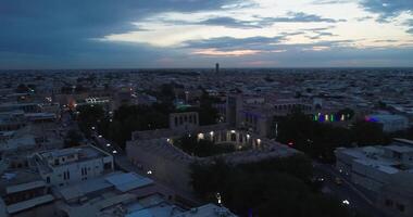 A drone flies over an ancient complex Lyab-i Hauz surrounded by houses in old Bukhara, Uzbekistan. Cloudy night. video
