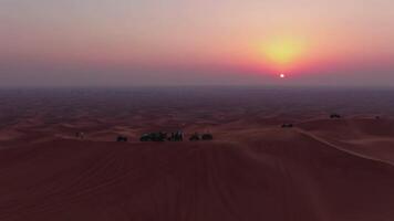 un' fuco mosche al di sopra di atvs in piedi su il sabbia dune di il deserto contro il fondale di il tramonto video