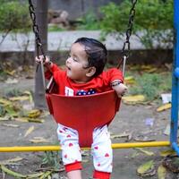 Smart Asian boy riding on swing in society park, happy boy play outdoors in summer, baby boy playing swing in the garden photo