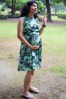 A pregnant Indian lady poses for outdoor pregnancy shoot and hands on belly, Indian pregnant woman puts her hand on her stomach with a maternity dress at society park, Pregnant outside maternity shoot photo