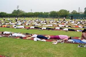 New Delhi, India, June 21, 2023 - Group Yoga exercise session for people at Yamuna Sports Complex in Delhi on International Yoga Day, Big group of adults attending yoga class in cricket stadium photo