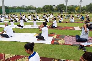 New Delhi, India, June 21, 2023 - Group Yoga exercise session for people at Yamuna Sports Complex in Delhi on International Yoga Day, Big group of adults attending yoga class in cricket stadium photo