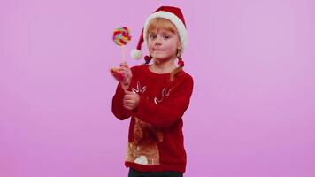 Joyful girl in Christmas sweater, hat holding candy striped lollipops, dancing, making silly faces video