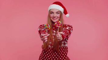 Joyful girl in red Christmas sweater, hat presenting candy striped lollipops, stretches out hands video