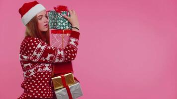 Girl in Christmas red sweater, Santa hat smiling, holding many gift boxes New Year presents shopping video