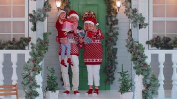 Senior grandmother grandfather with granddaughter standing at Christmas house porch waving hello hi video