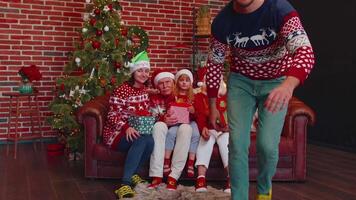 Man sets timer on mobile phone taking multigenerational family selfie portrait celebrating Christmas video