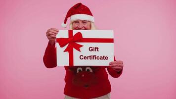 Senior grandmother woman in New Year sweater presenting card gift certificate coupon winner voucher video