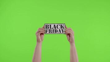 Black Friday advertisement inscription on paper sheet in womans hands on chroma key. Slow motion video