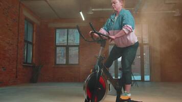 athlétique femme équitation sur filage Stationnaire bicyclette formation routine dans brume salle de sport, poids perte à l'intérieur video