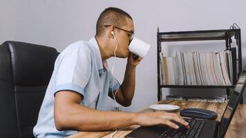 a man drinking from a cup. person having a coffee in front of him while he works. photo