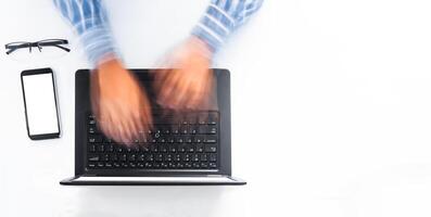 overhead shot of a man's hands typing fast on a laptop on a white desk. programming concept. office work. photo