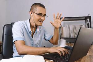 young latinx man raises his hand in front of his computer. student in a video chat on a laptop photo