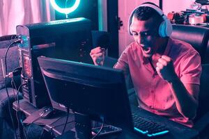 Portrait of a young latinx holding arms making a winner gesture in front a gamer personal computer. photo