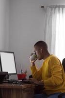 Hispano hombre Bebiendo desde un taza trabajando en un computadora foto