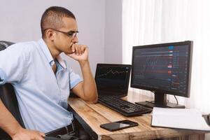 joven Hispano hombre visita un grafico en un computadora. latinx hombre invierte en el valores mercado y estudios comerciante. foto