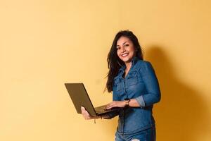 Portrait of happy young woman holding laptop smiling look camera over yellow background. photo