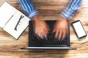 overhead shot of a man's hands typing quickly on a laptop. online assistance concept photo