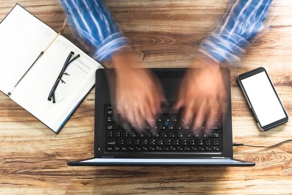 overhead shot of a man's hands typing quickly on a laptop. online assistance concept