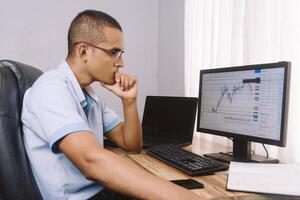 Young latinx man studying trading on his computer. Student learning to invest. technology and bitcoin. photo