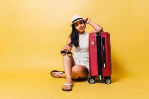 Woman with hat and a suitcase sitting over yellow background. photo