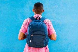 man from behind with a backpack in front of a blue wall. photo
