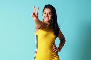 cheerful young latinx woman look at camera doing victory sign, peace concept. photo