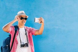 latín americano sonriente vistiendo lentes y sombrero tomando un selfie foto