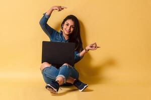 Latinx woman sitting on floor using a laptop pointing with hands and fingers to the side copy space. photo