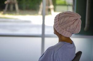 Asian woman with cancer, sitting with her back turned and looking out the window photo