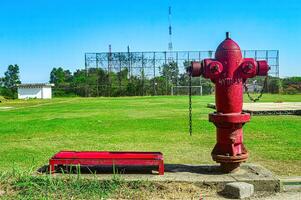 Red and silver fire hydrant against a green grass football field in the background on a hot day, Indonesia, 17 July 2023. photo