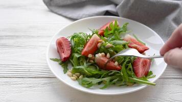 een vrouw hand- picks een aardbei en rucola salade met een vork video